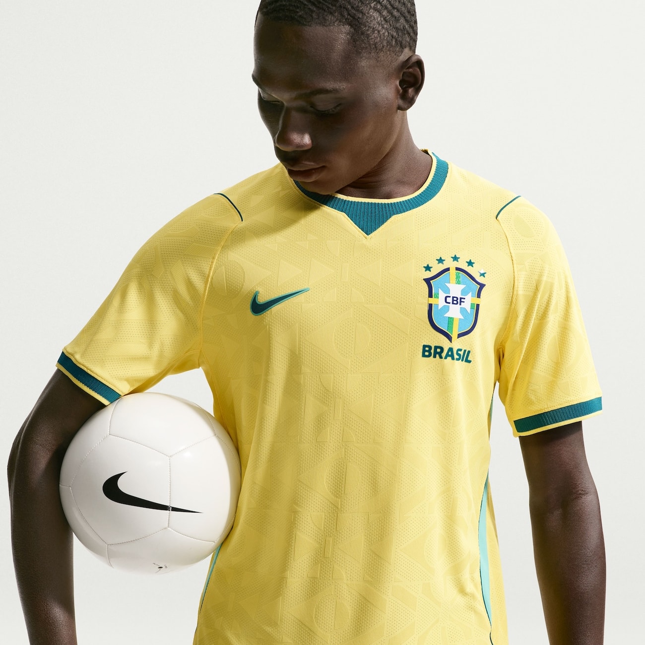 Modelo vestindo a camisa amarela do Brasil e segurando uma bola branca